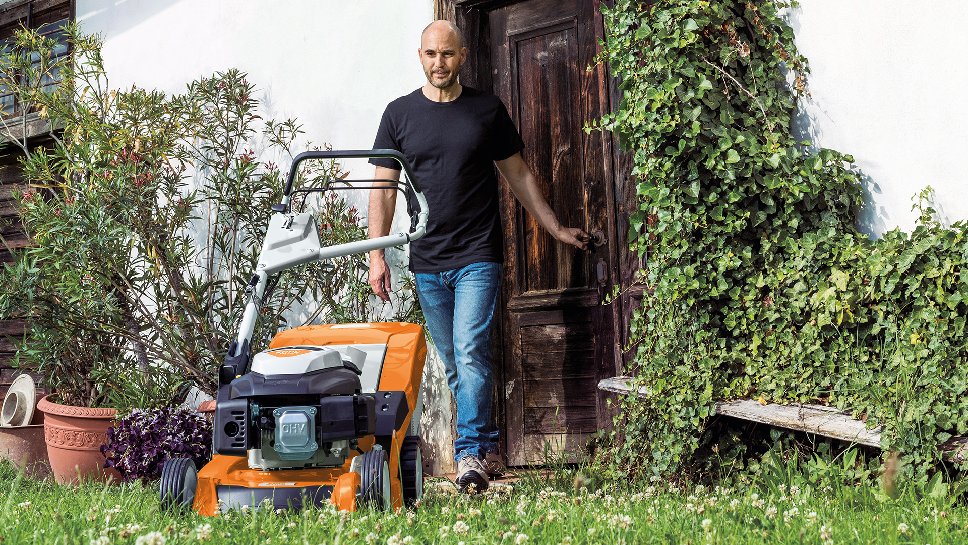 Homem a sair de uma porta para o espaço verde até ao corta-relva a gasolina STIHL RM 650