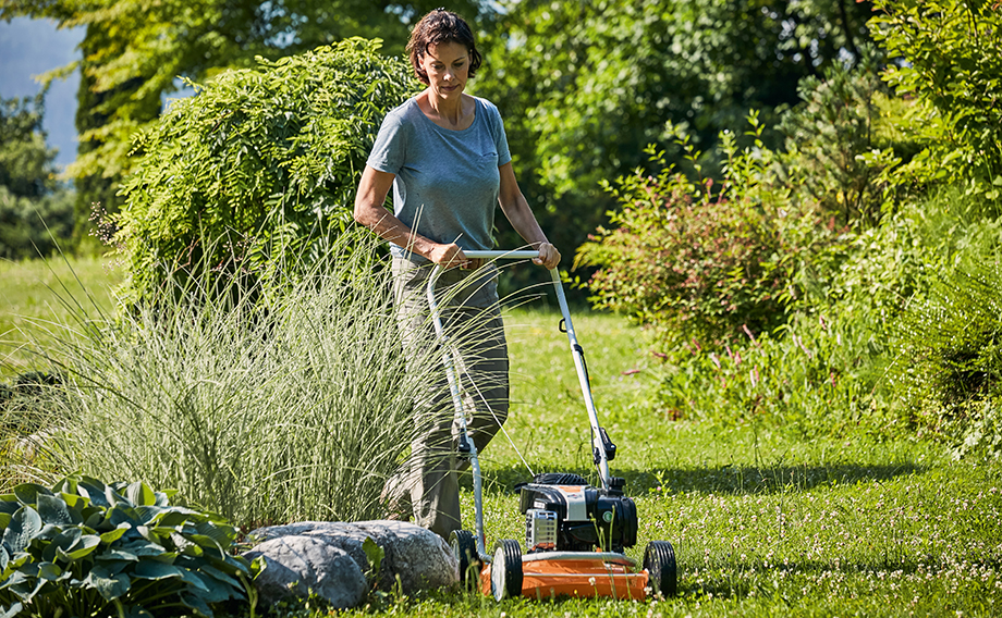 Uma mulher a cortar a relva num jardim no verāo com um corta-relva com função de mulching STIHL RM 2 R