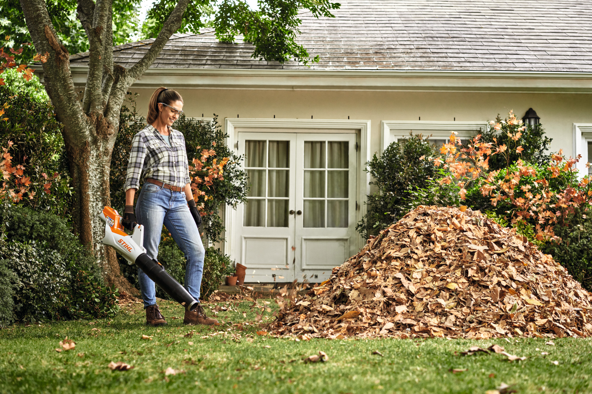 Uma mulher limpa folhas num espaço verde com a ajuda de um soprador a bateria STIHL BGA 60