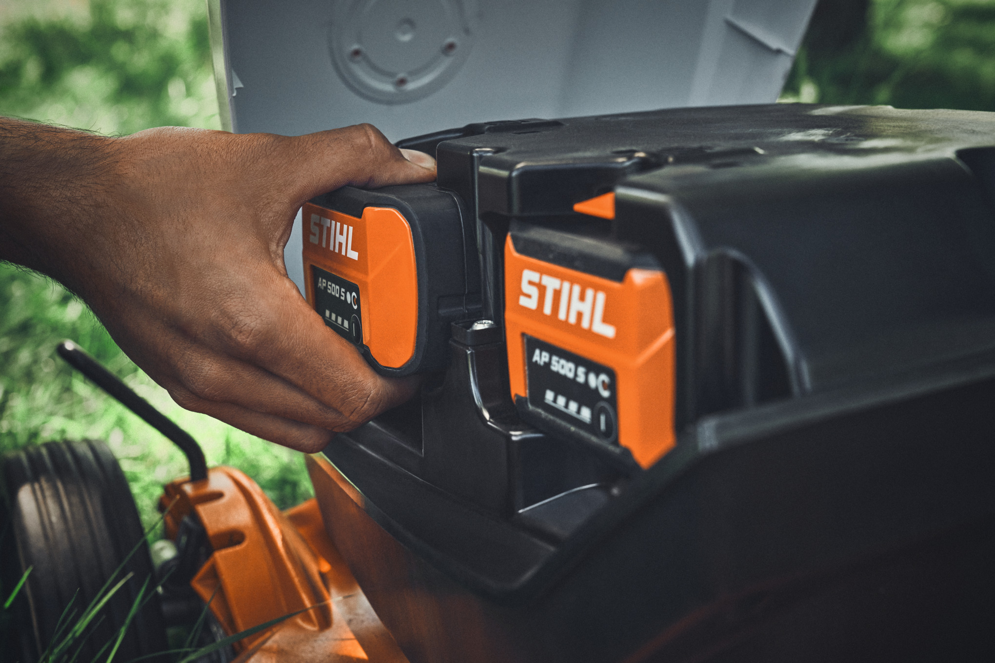 Uma pessoa insere uma bateria STIHL AP 500 S num cortador de relva a bateria STIHL