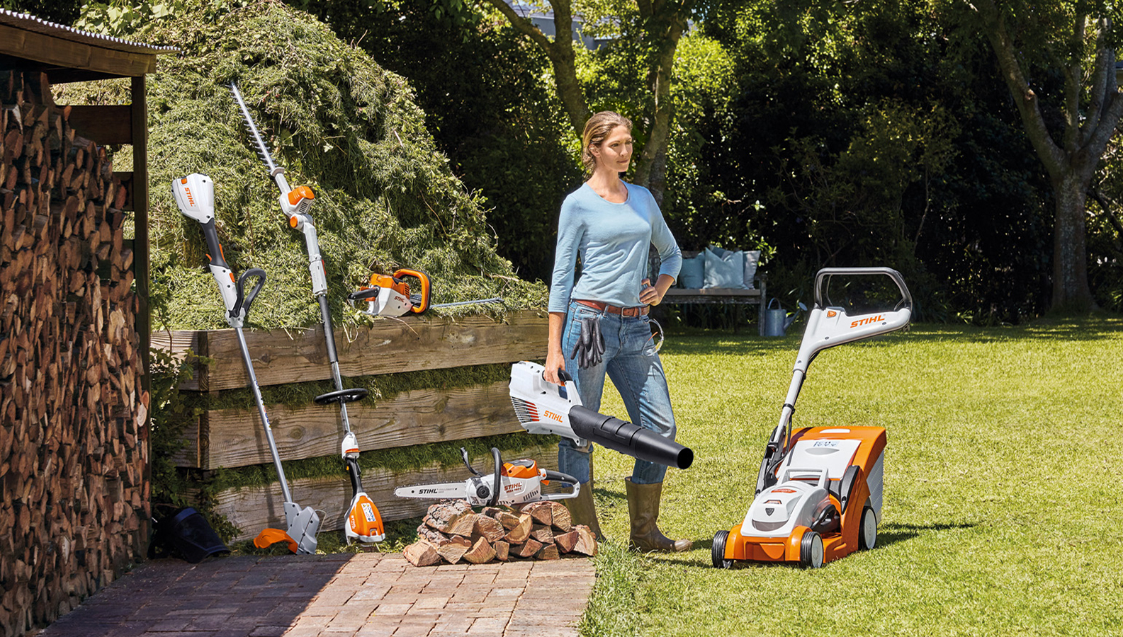 Mulher de pé no jardim com uma selecção de produtos de pilhas da STIHL