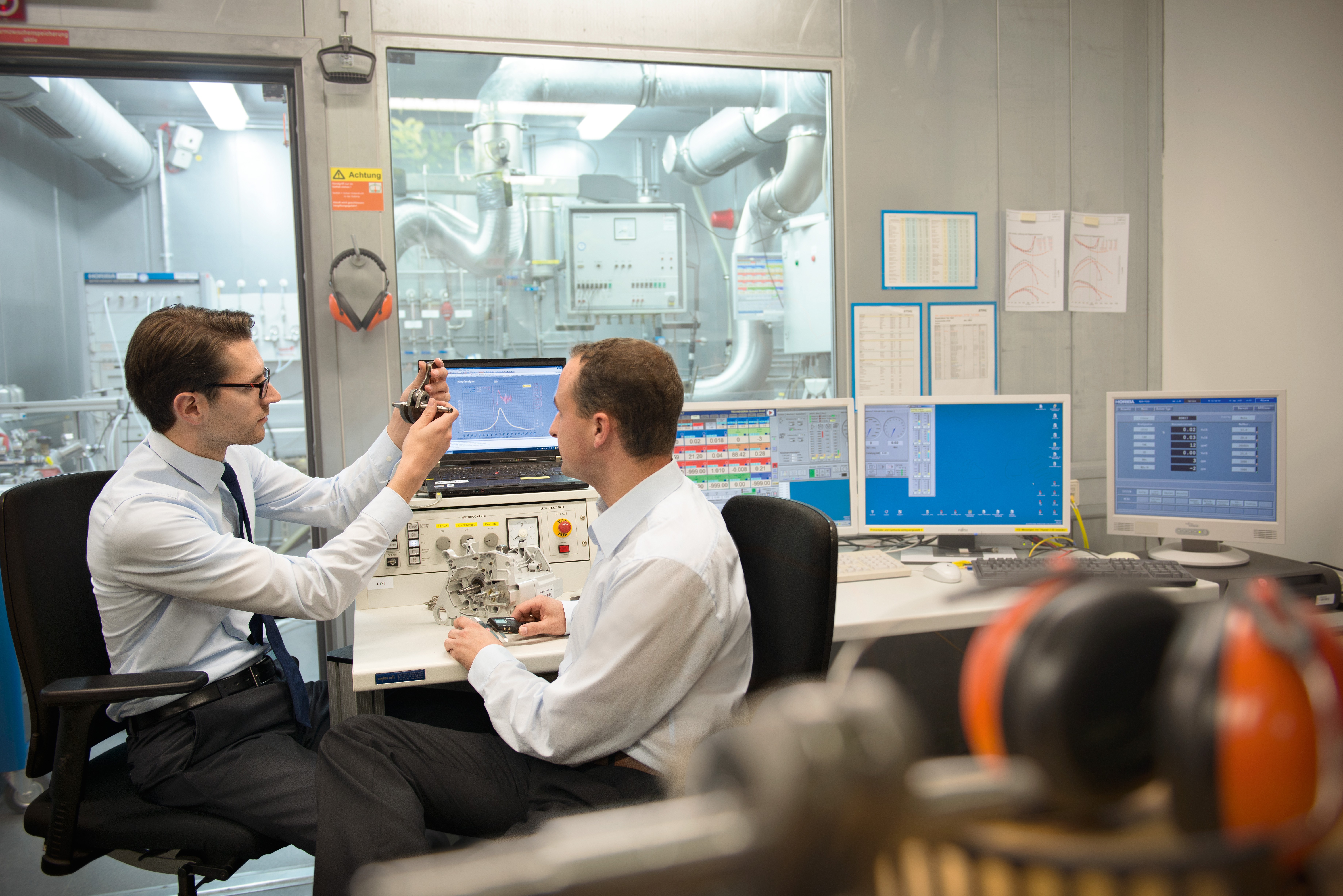 Dois homens sentados num laboratório de inovação STIHL, diante ecrãs, examinando uma parte de um novo produto.