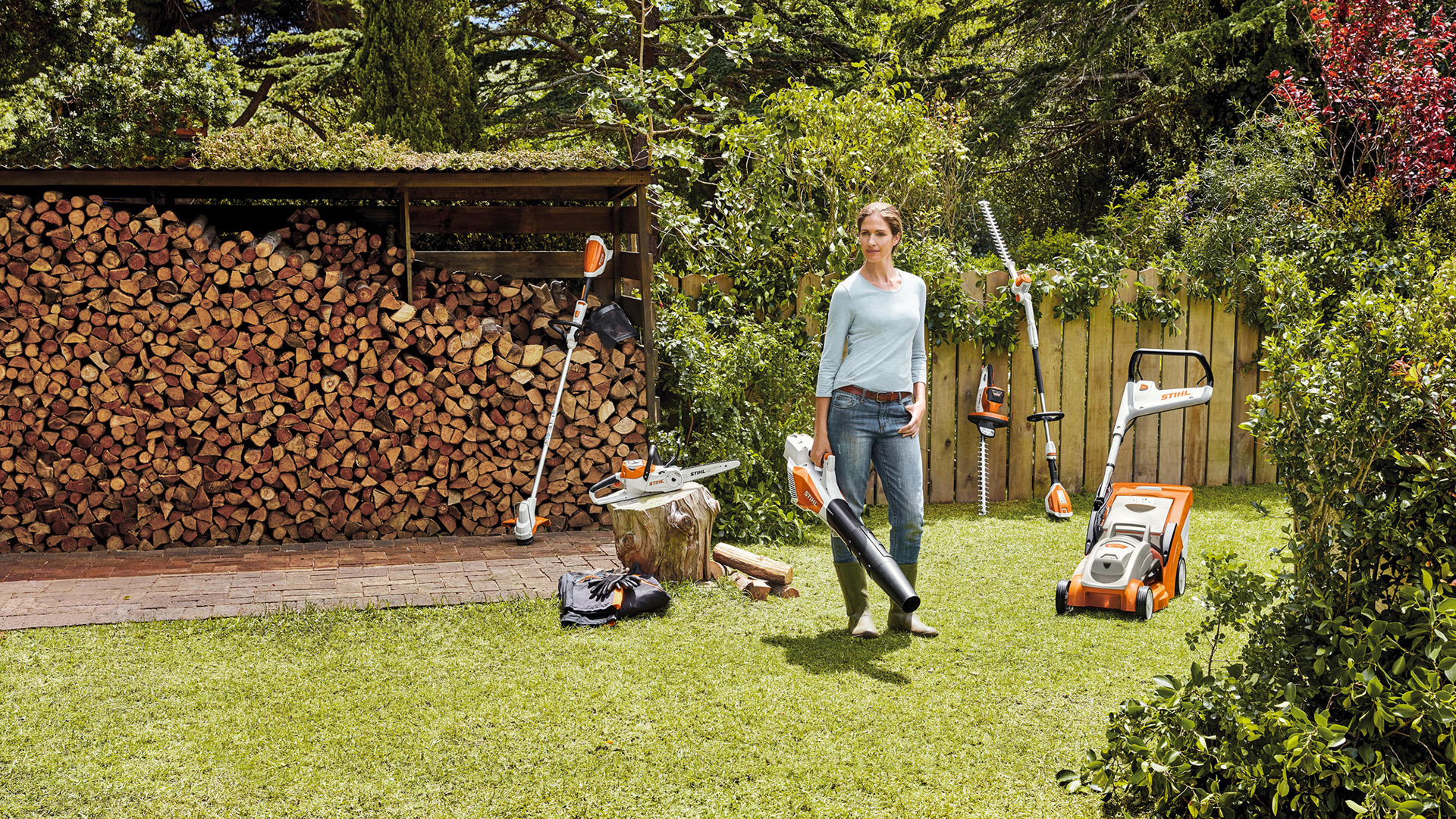 Uma mulher num jardim com uma seleção de máquinas a bateria do sistema STIHL AK