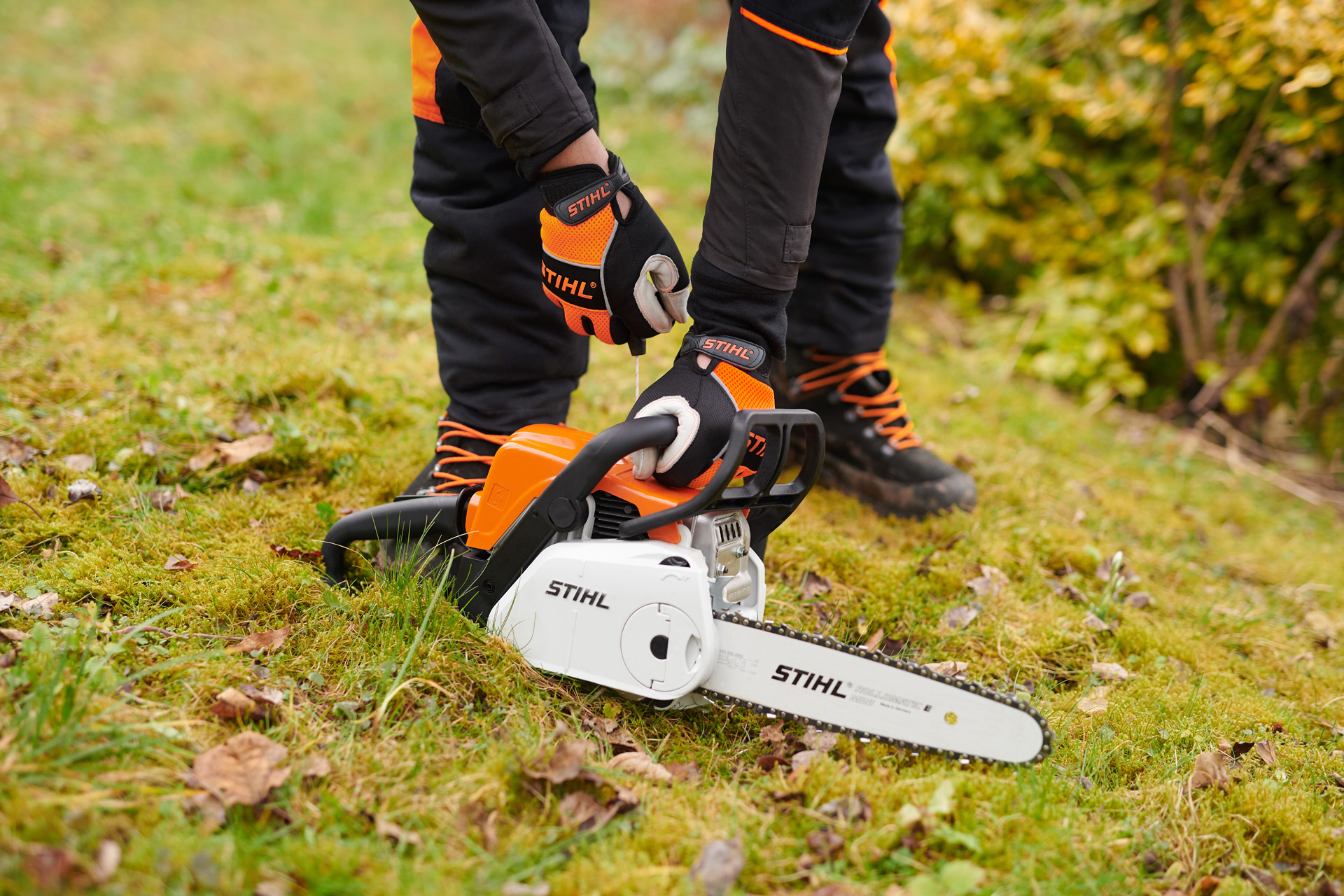 Uma motosserra STIHL MS 180 C-BE a gasolina com o sistema STIHL ErgoStart sobre relva, durante o arranque