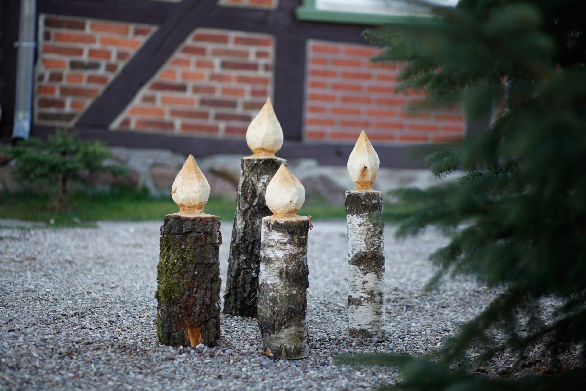 Quatro castiçais de bricolage em madeira num caminho ao lado de um abeto