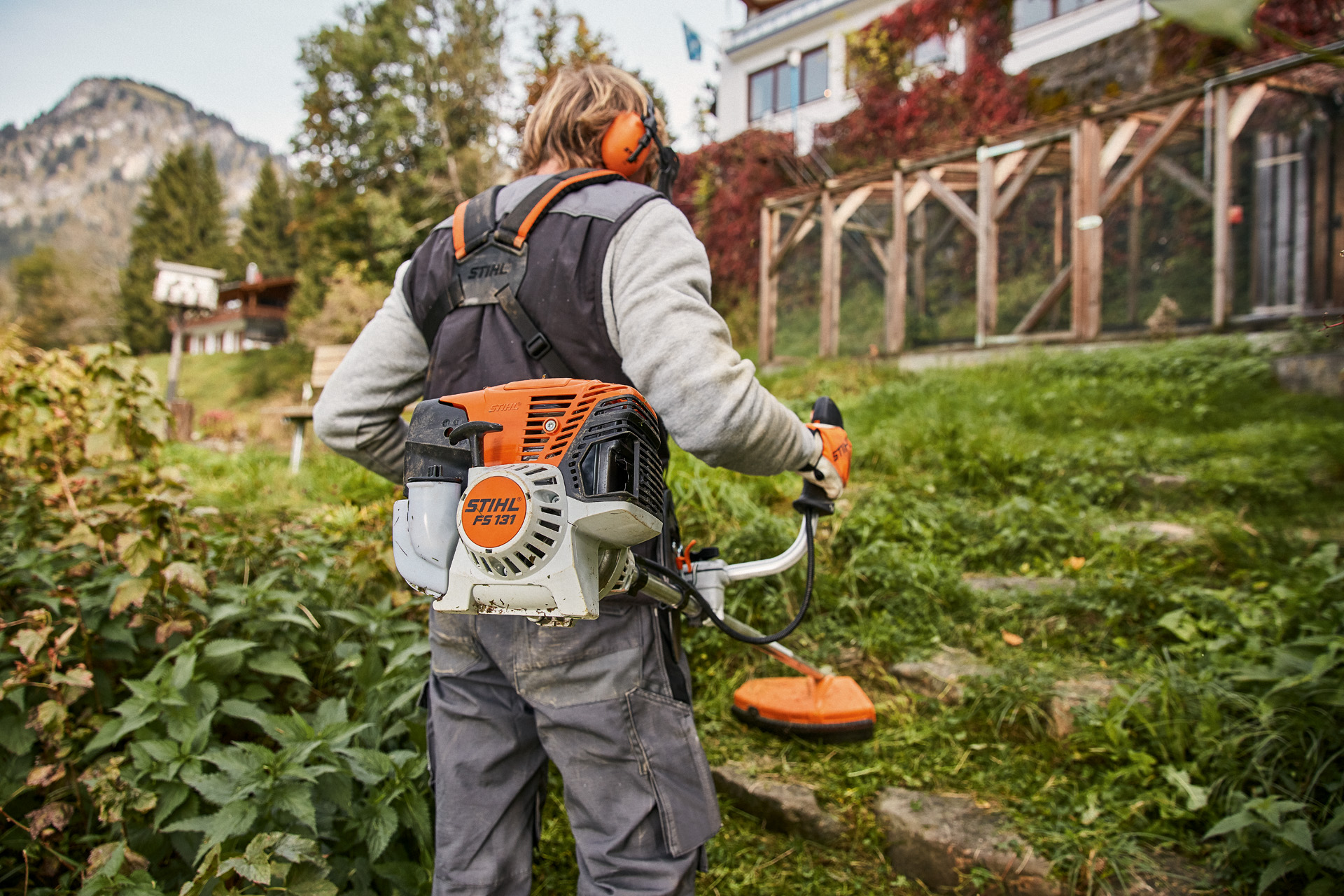 Pessoa usa uma foice com motor STIHL 4-MIX® FS 131 a gasolina em terreno relvado irregular à frente de uma casa