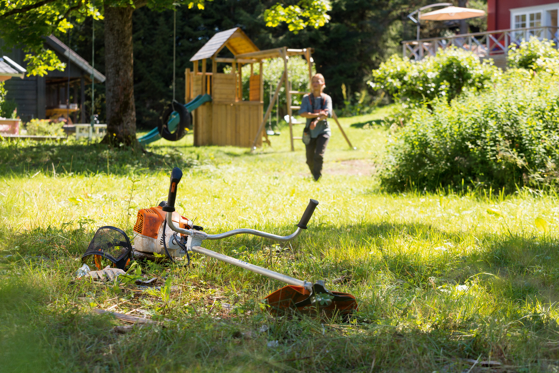 Uma foice a motor STIHL FS 240 no chão de um jardim e um homem a aproximar-se da máquina.