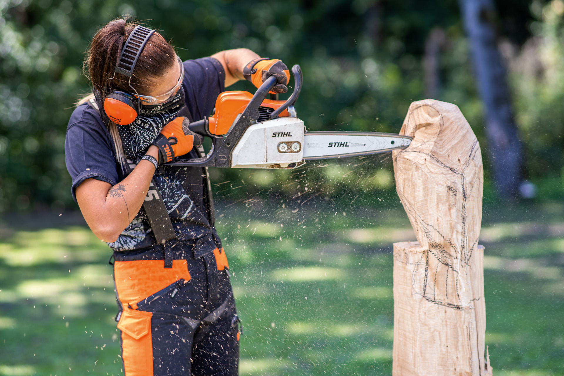 Uma mulher a usar equipamento de proteção a esculpir uma coruja em madeira com uma motosserra - escultura com motossera
