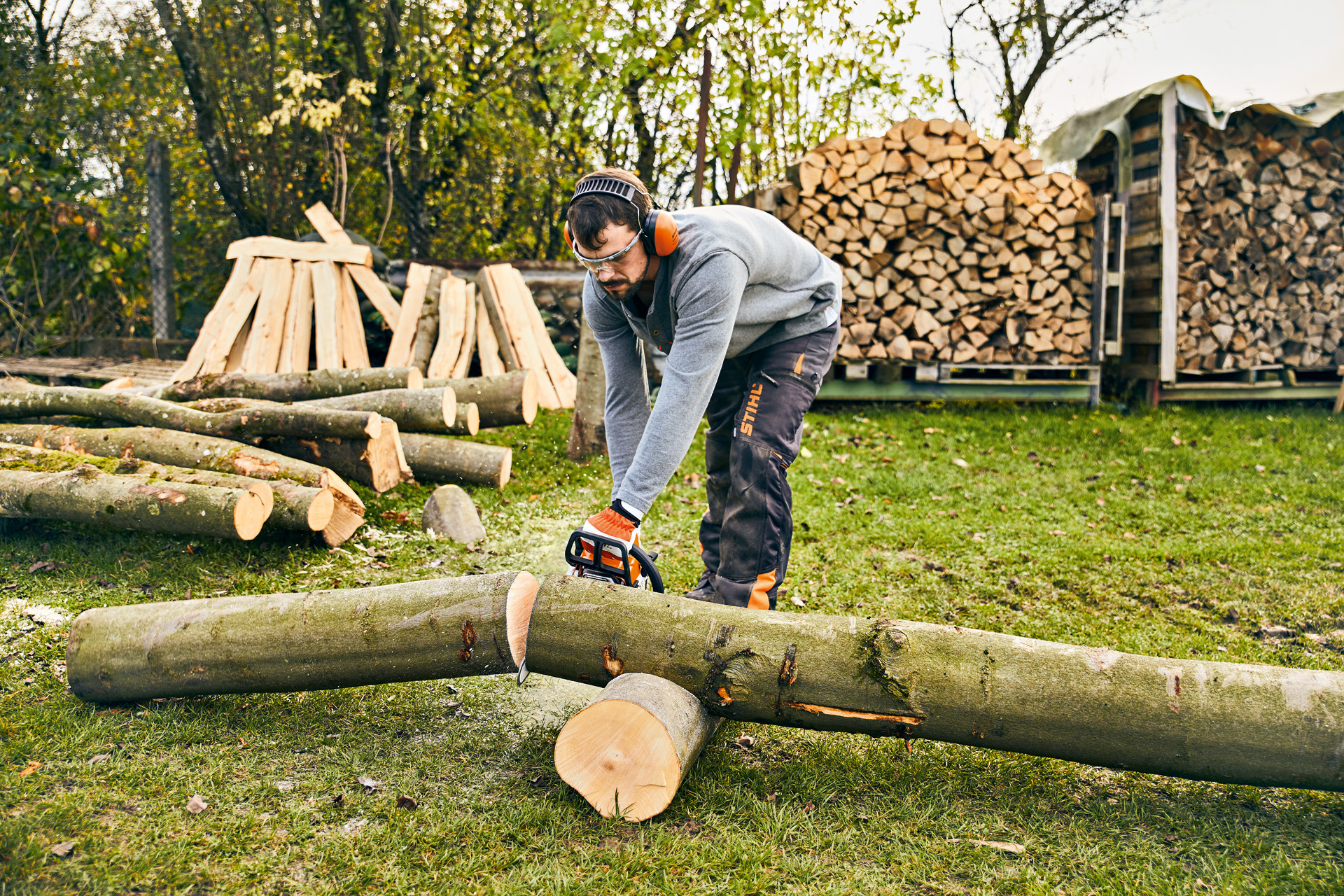 Um homem prepara a sua bricolage de mobiliário para espaços verdes ao serrar um tronco com uma motosserra STIHL MS 180