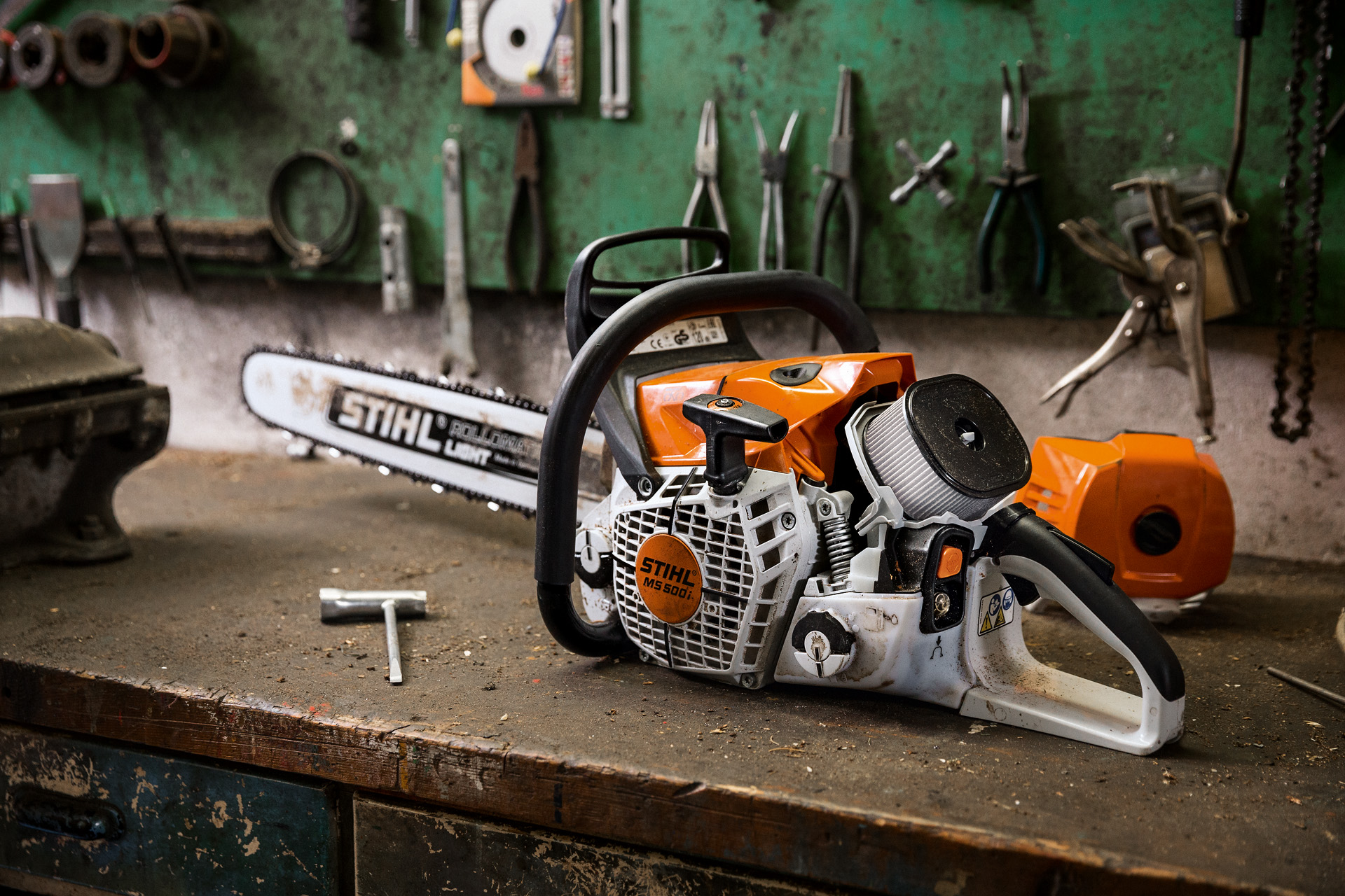 Uma motosserra a gasolina STIHL MS 500i W sobre uma mesa, com ferramentas na parede