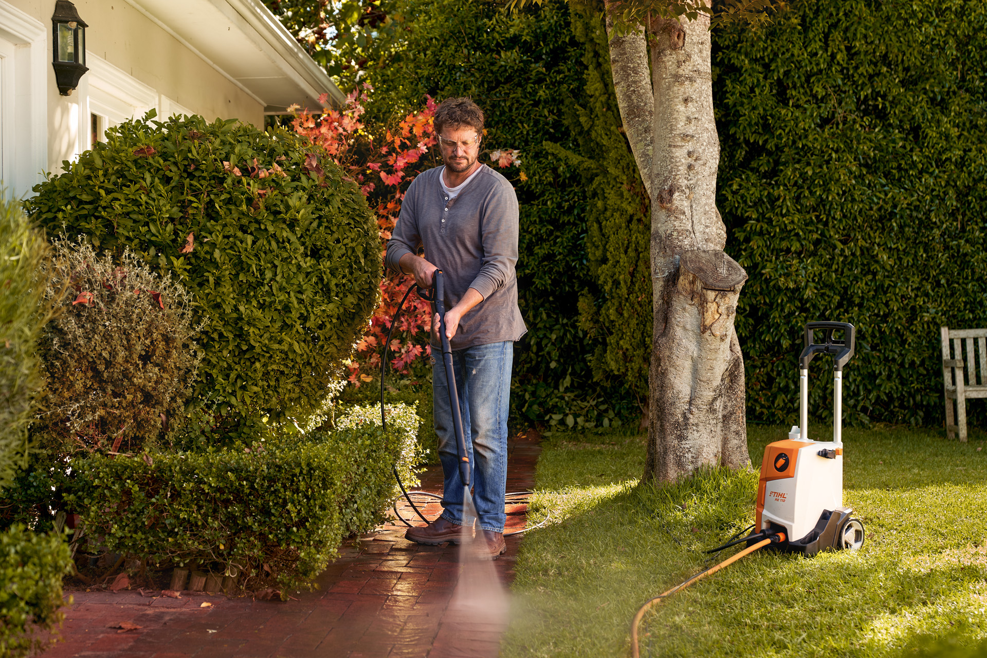 Um homem faz a limpeza das pedras do pavimento à frente da casa com uma máquina de limpeza de alta pressão STIHL RE 110