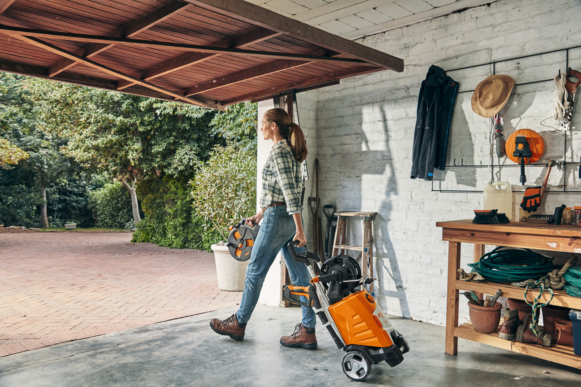 Uma mulher sai de uma garagem com a lavadora de alta pressão STIHL RE 130 PLUS para a usar