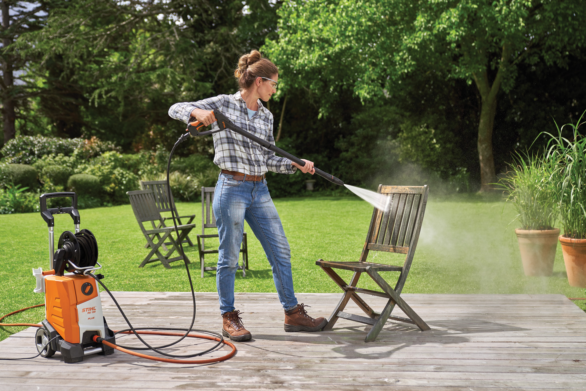 Uma mulher a usar uma máquina de limpeza de alta pressão STIHL RE 130 Plus para limpar uma cadeira de madeira para jardins num pátio