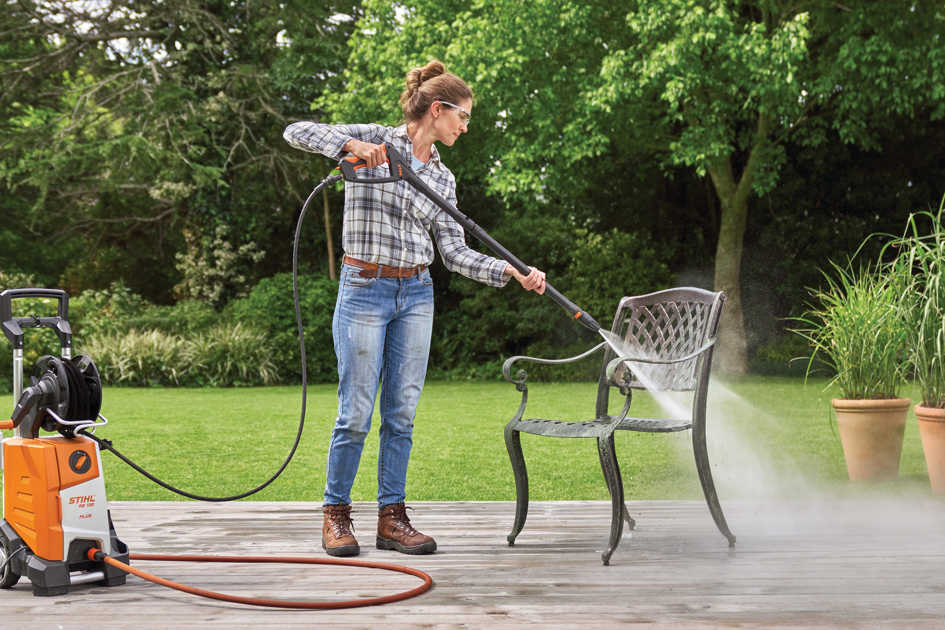 Uma mulher a utilizar a máquina de limpeza de alta pressão STIHL RE 130 Plus numa cadeira de metal num pátio num jardim