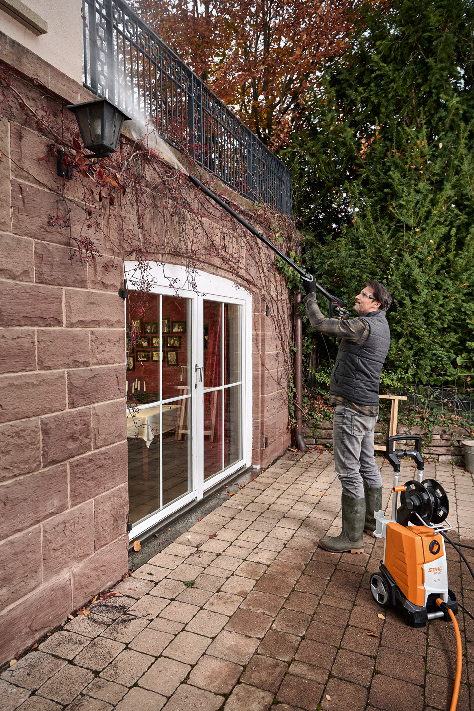 Um homem num terraço a limpar o exterior de uma casa com uma lavadora de alta pressão STIHL