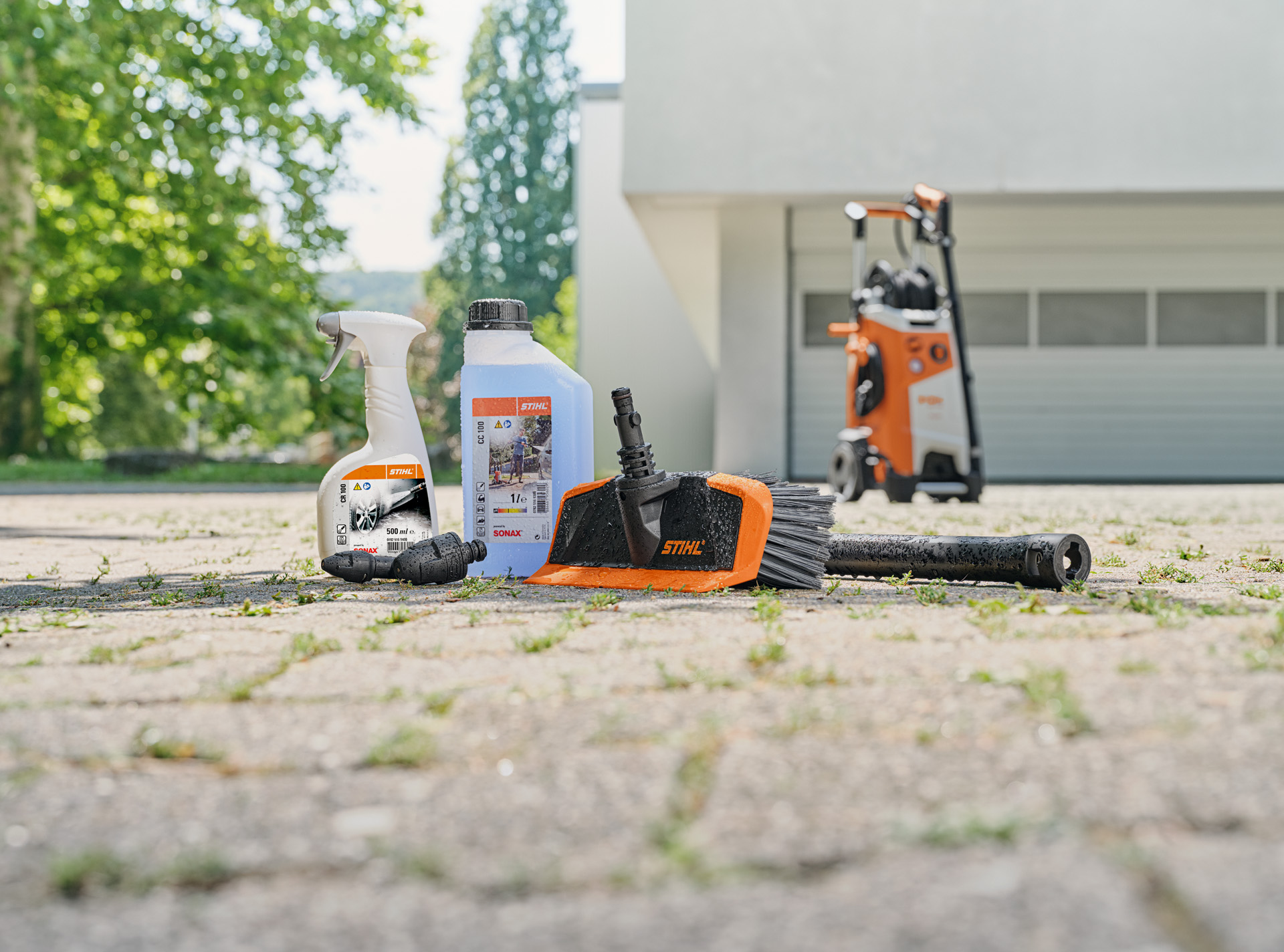 Detergente para jantes, champô para viaturas e escova de lavagem da STIHL no chão à frente duma garagem branca.