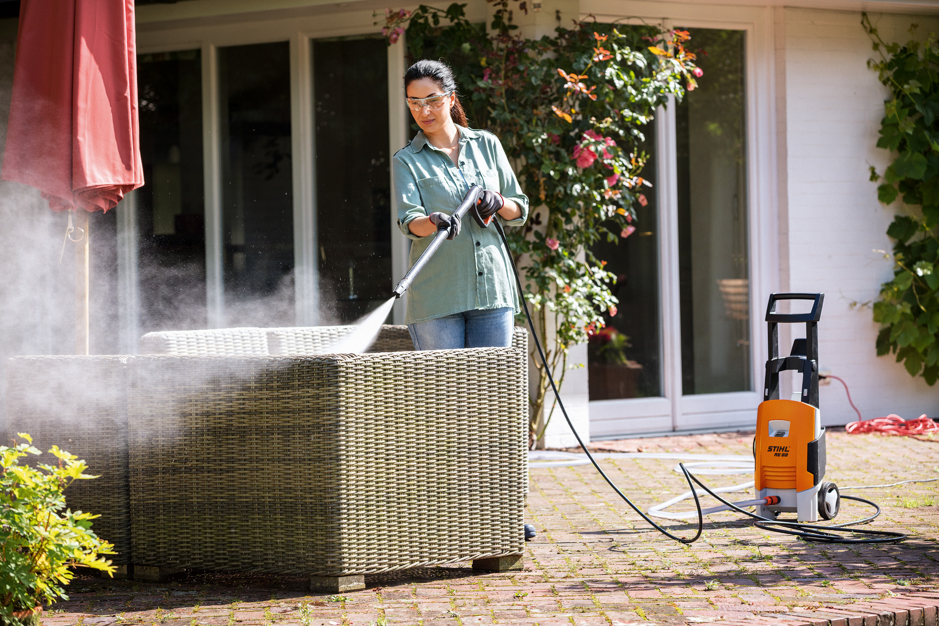 Mulher a limpar cadeiras de jardim de madeira no seu terraço com um STIHL RE 130 mais detergente de alta pressão