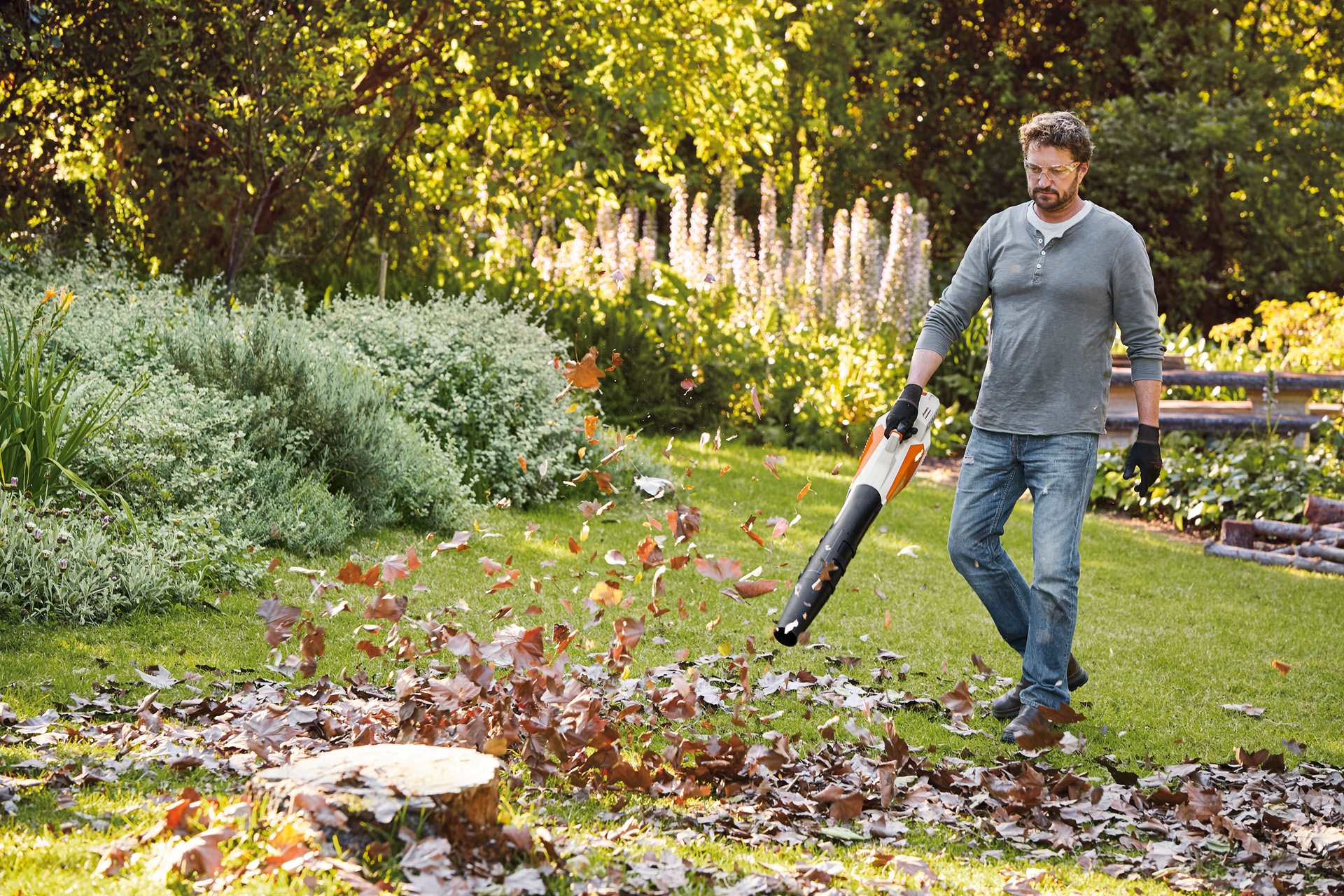 Um homem a soprar folhas num jardim com um soprador de mão a bateria STIHL BGA 57