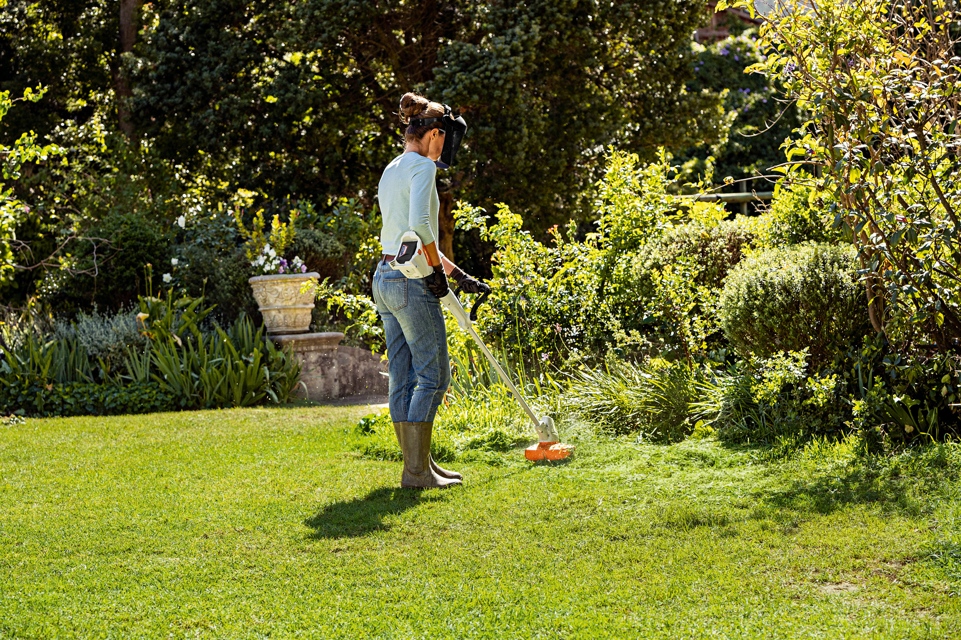 Uma mulher a cortar os rebordos de um relvado com a aparadora STIHL FSA 57