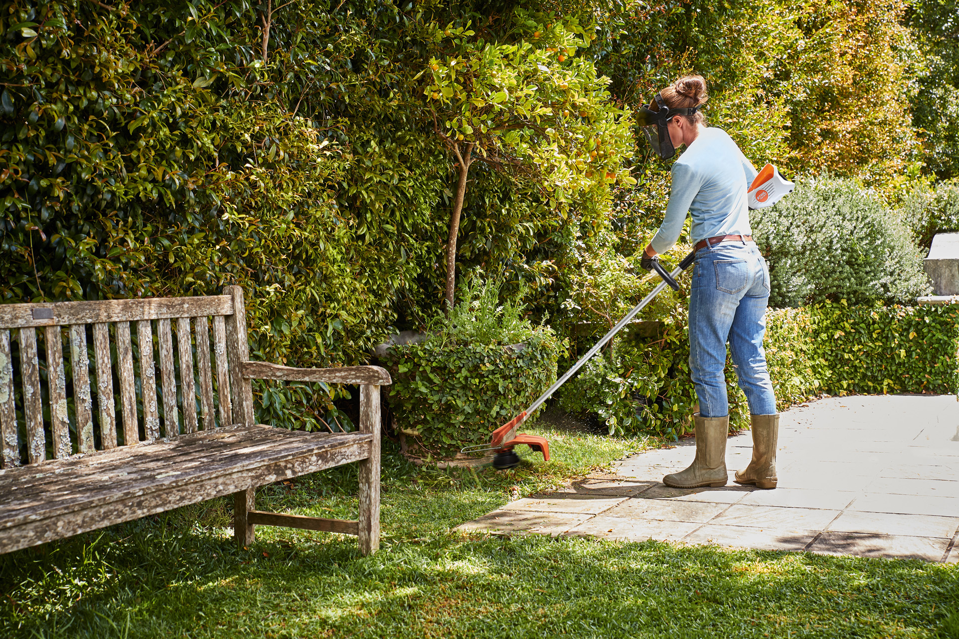 Uma mulher a cortar relva à volta de uma árvore pequena com uma aparadora a bateria STIHL FSA 60 R