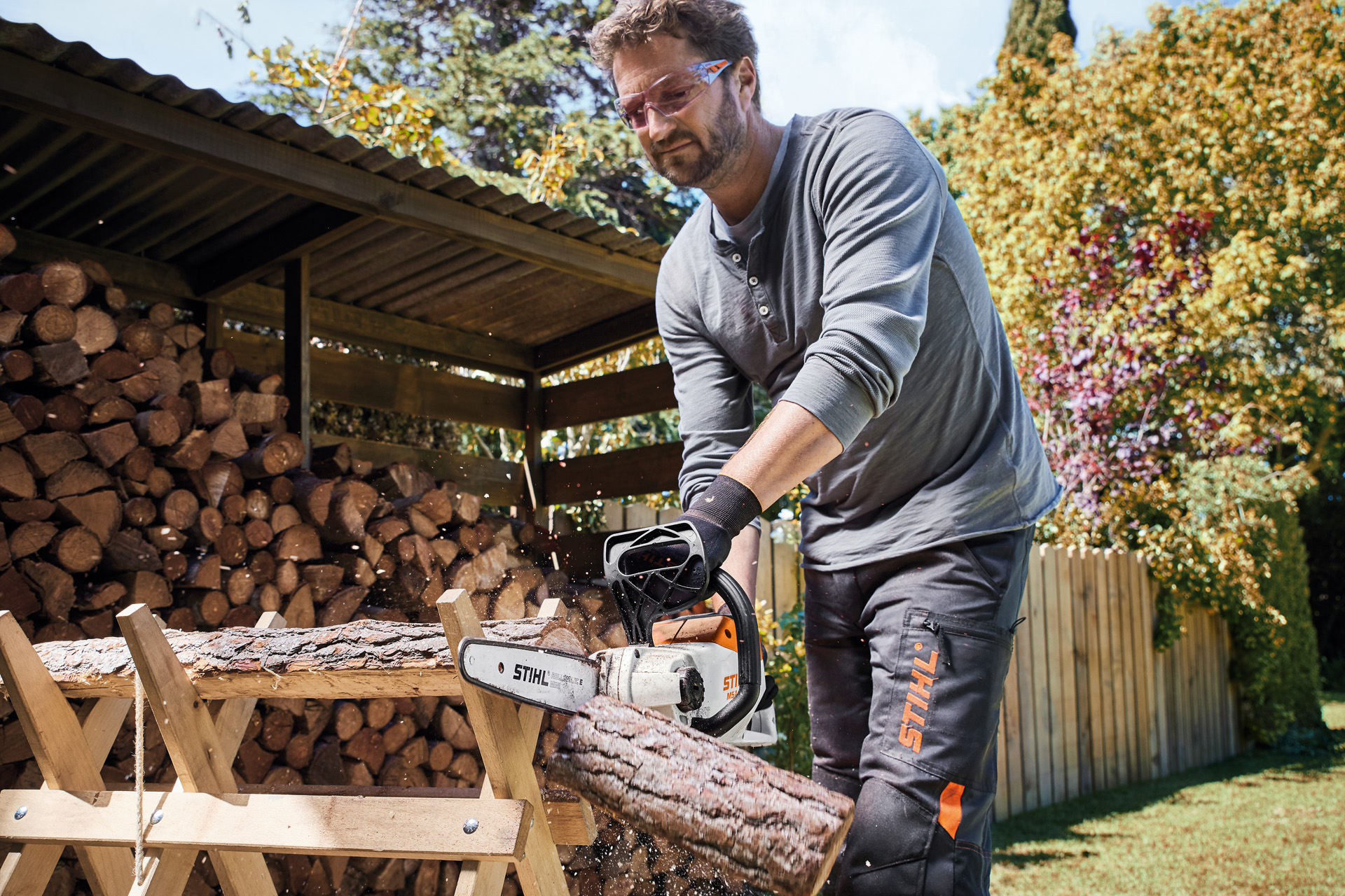 Um homem com óculos de segurança a serrar um tronco com uma motosserra a bateria STIHL MSA 140 C-B