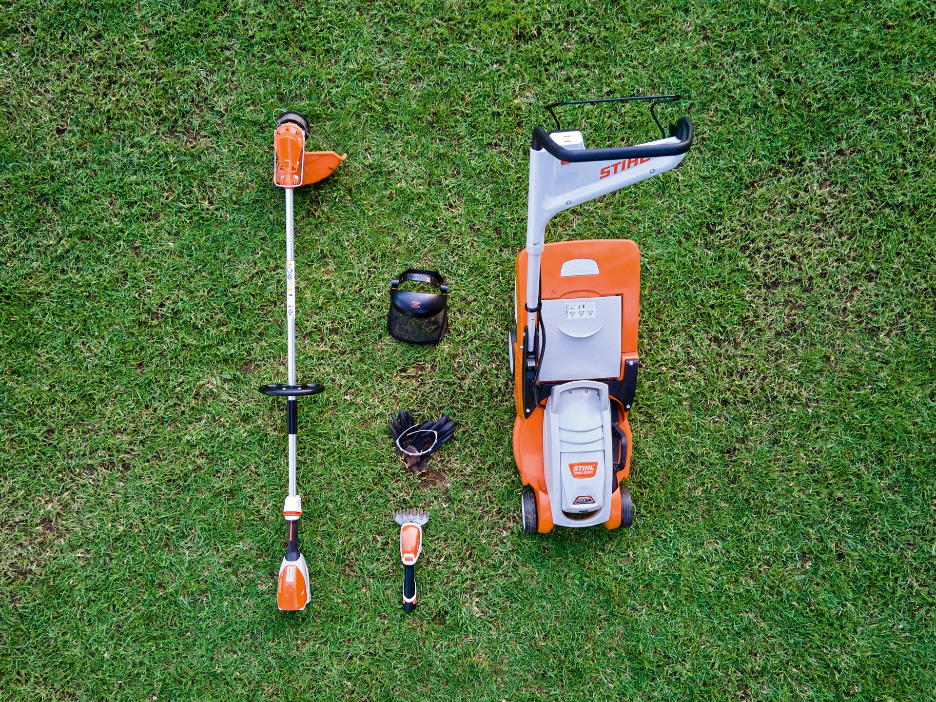 Um corta-relva STIHL, uma motorroçadora e uma minipodadora a bateria HSA&nbsp;26 sobre um relvado