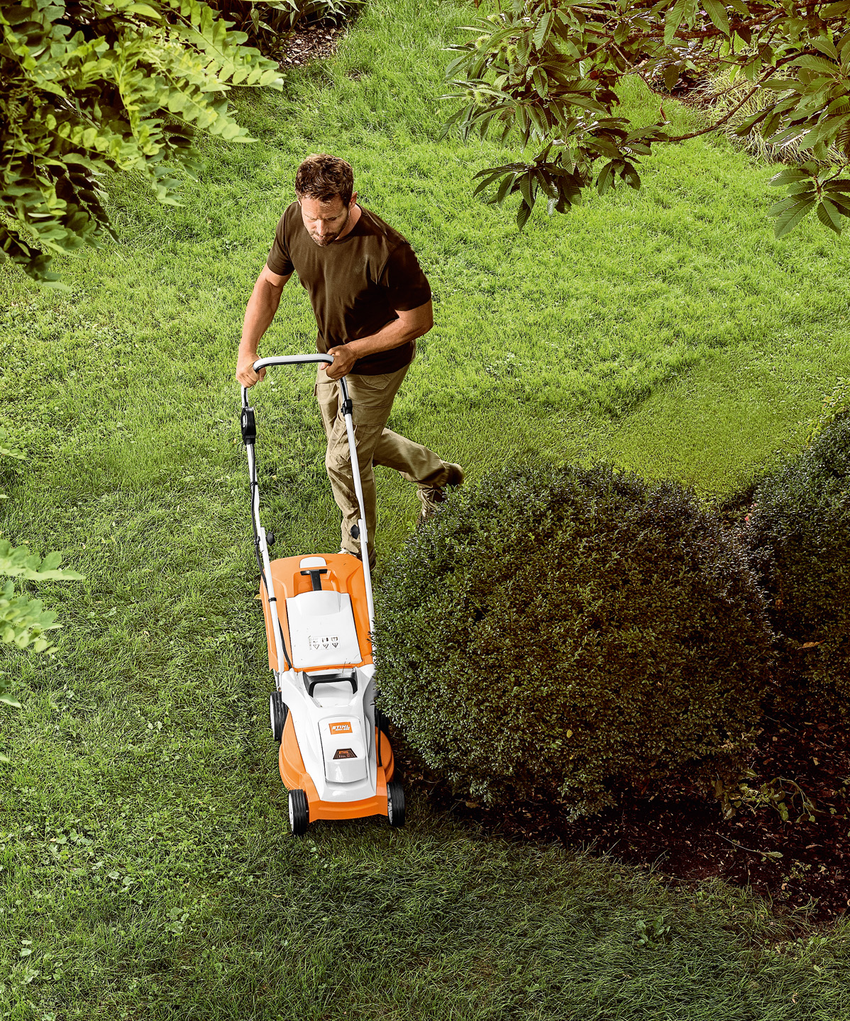 Vista de cima: um homem corta uma área relvada à volta de uma árvore pequena com o corta-relva a bateria STIHL RMA 235.