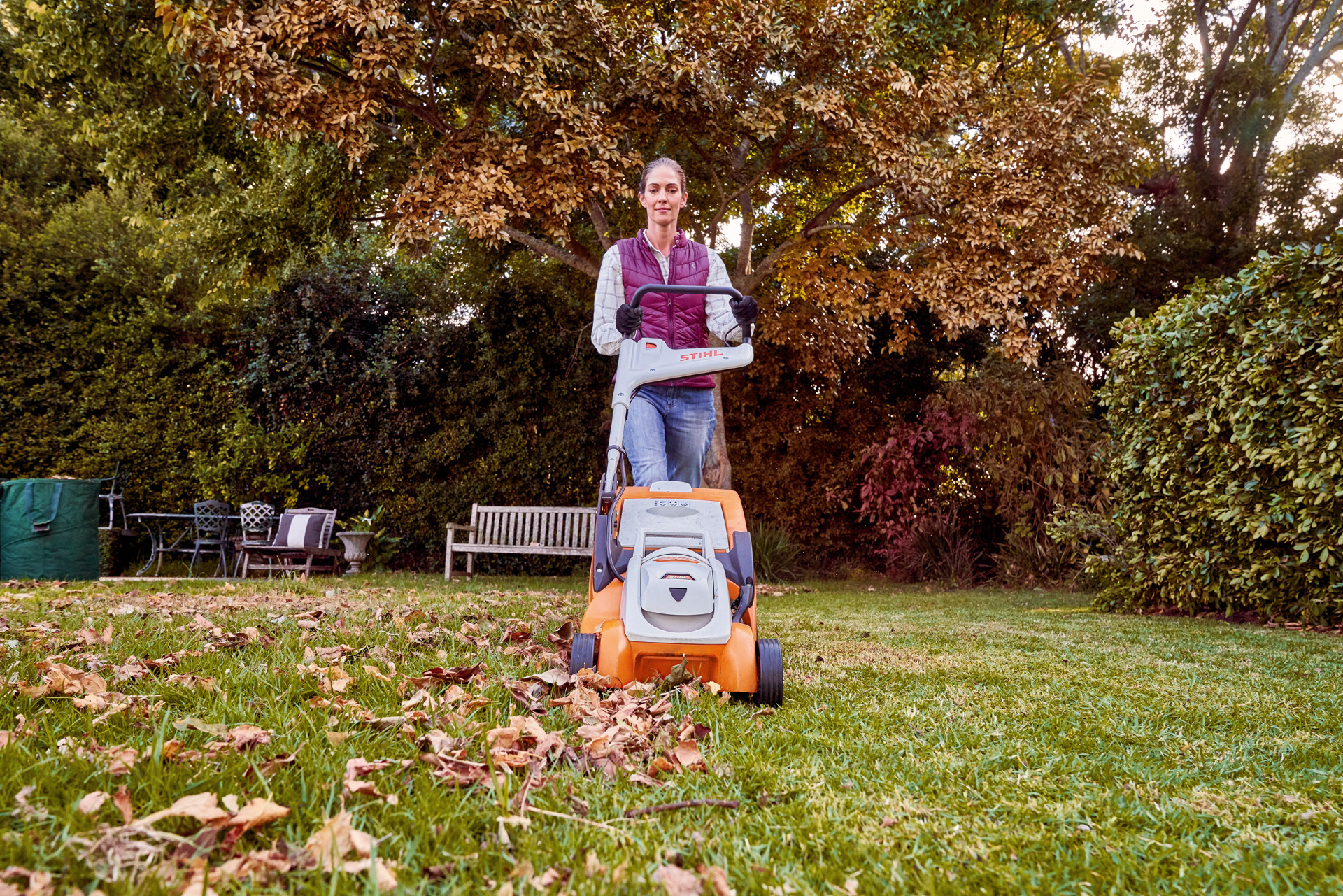 Mulher aplica os cuidados com a relva no outono ao usar um corta-relva a bateria STIHL RMA 339 C num espaço verde