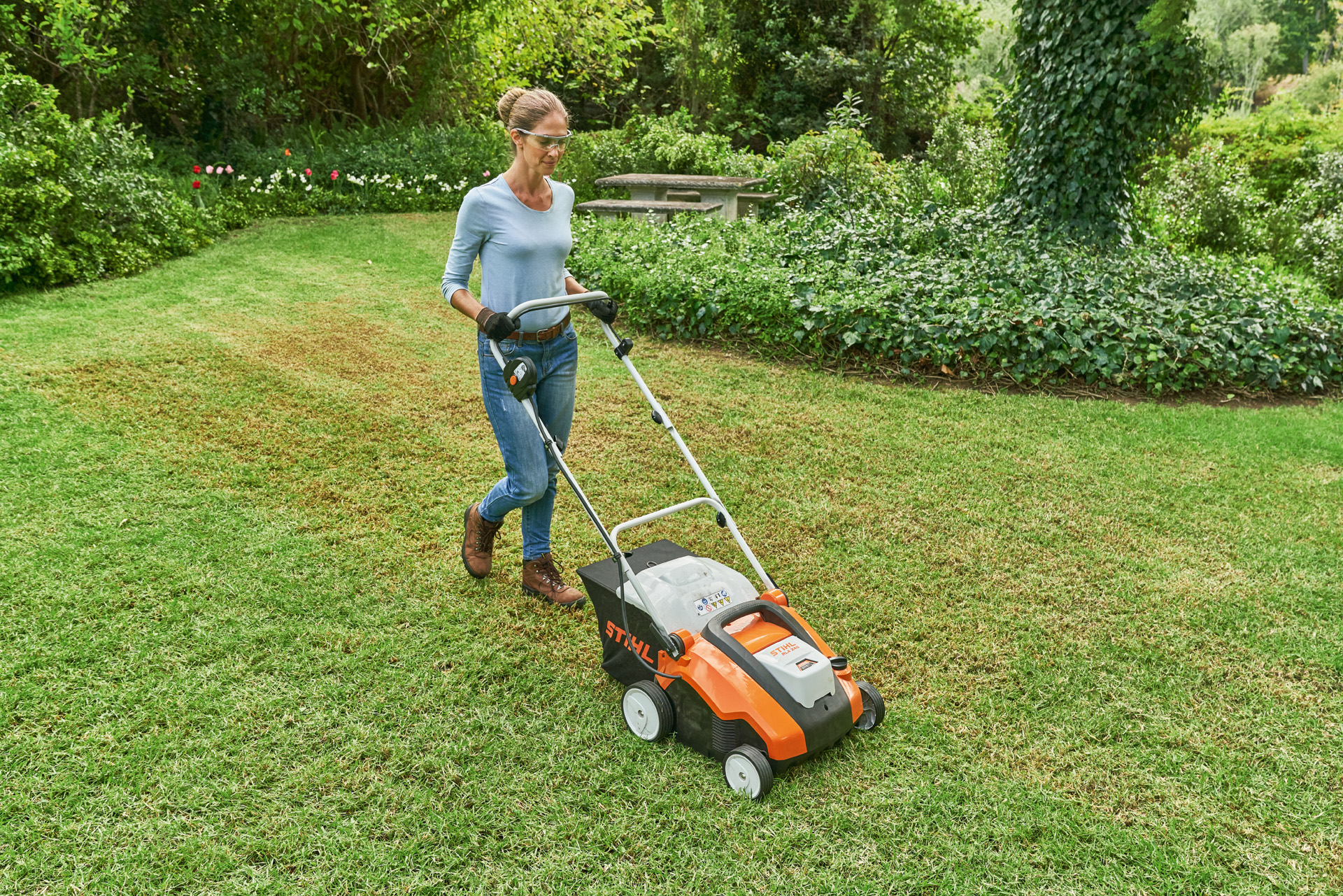 Uma mulher com equipamentos de proteção escarifica uma área relvada pequena com um arejador de relva STIHL RLA 240.