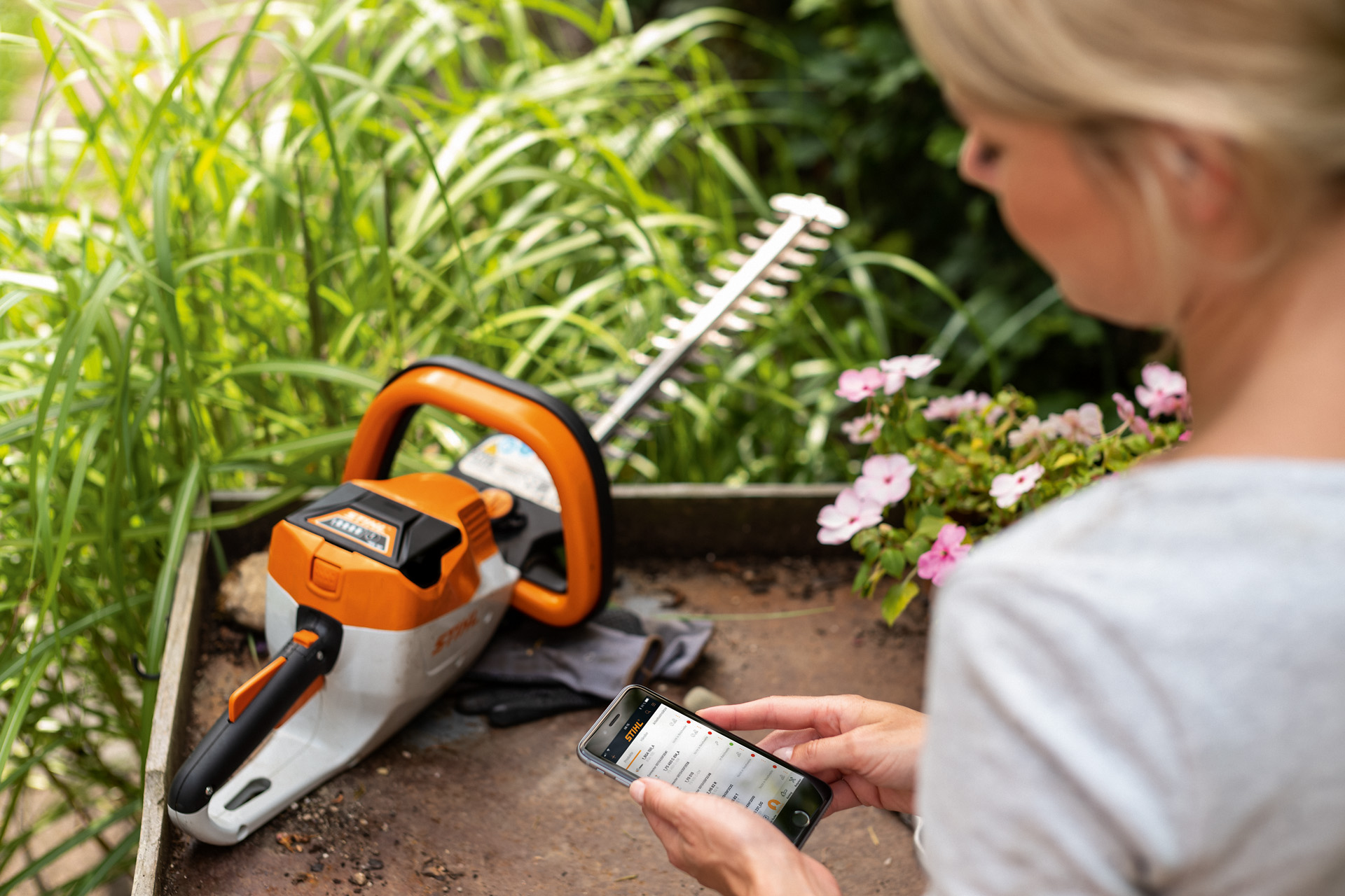 Uma mulher regista a sua podadora de sebes STIHL através da aplicação STIHL num smartphone