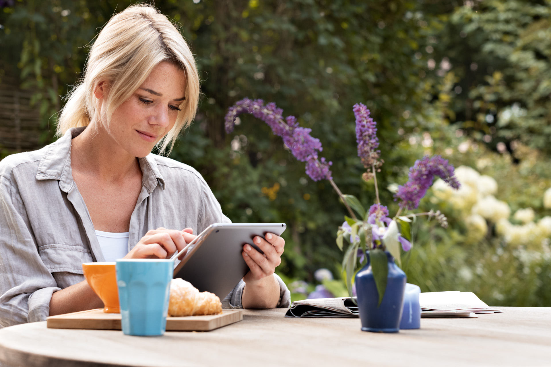 Uma mulher a usar o tablet à mesa do pequeno-almoço no jardim