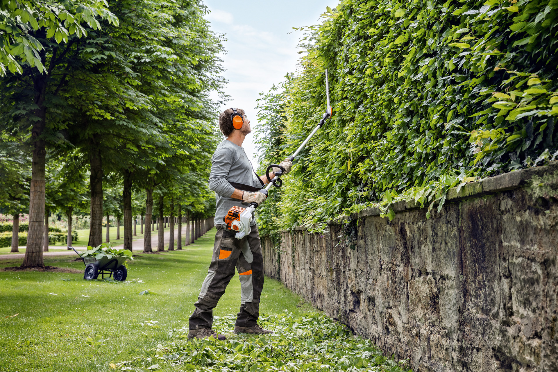 Um homem envergando vestuário de proteção apara a face vertical de uma sebe alta com uma podadora STIHL HL 94.