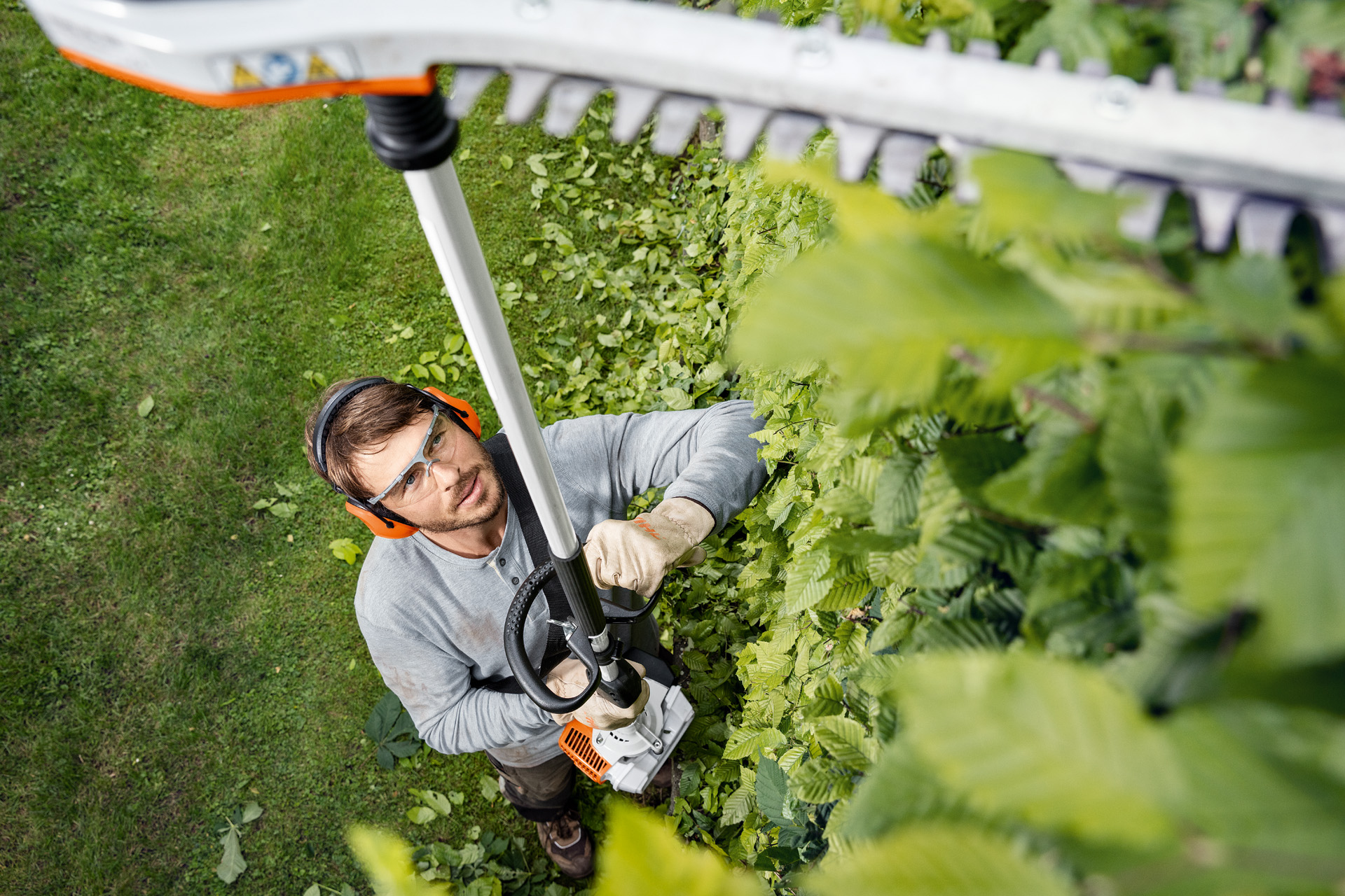 Um homem com vestuário de proteção apara sebes altas com uma podadora de sebes STIHL HL 94.