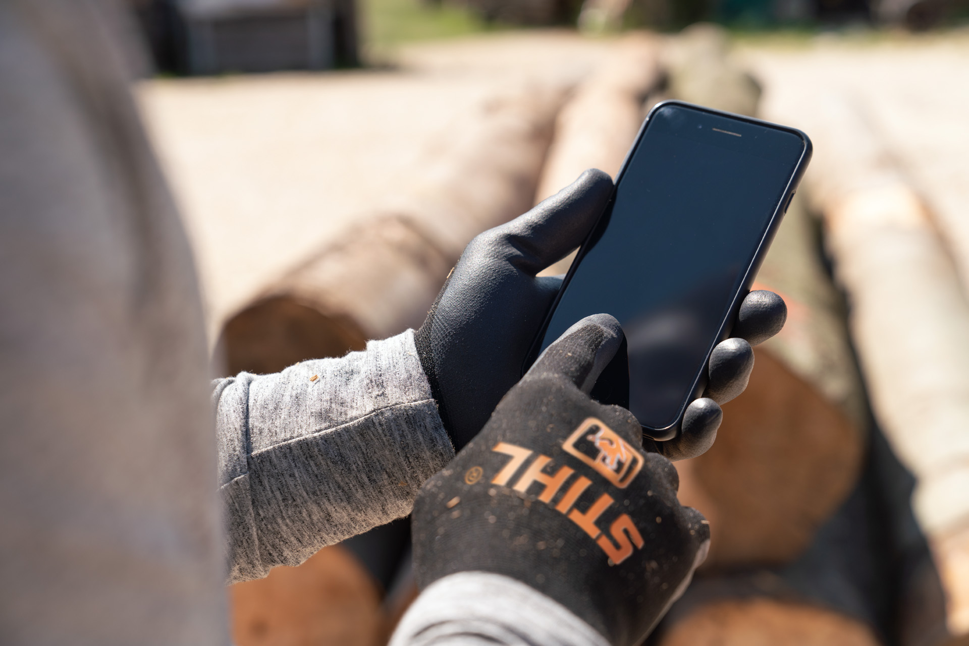 Um homem com luvas de proteção STIHL toca no smartphone