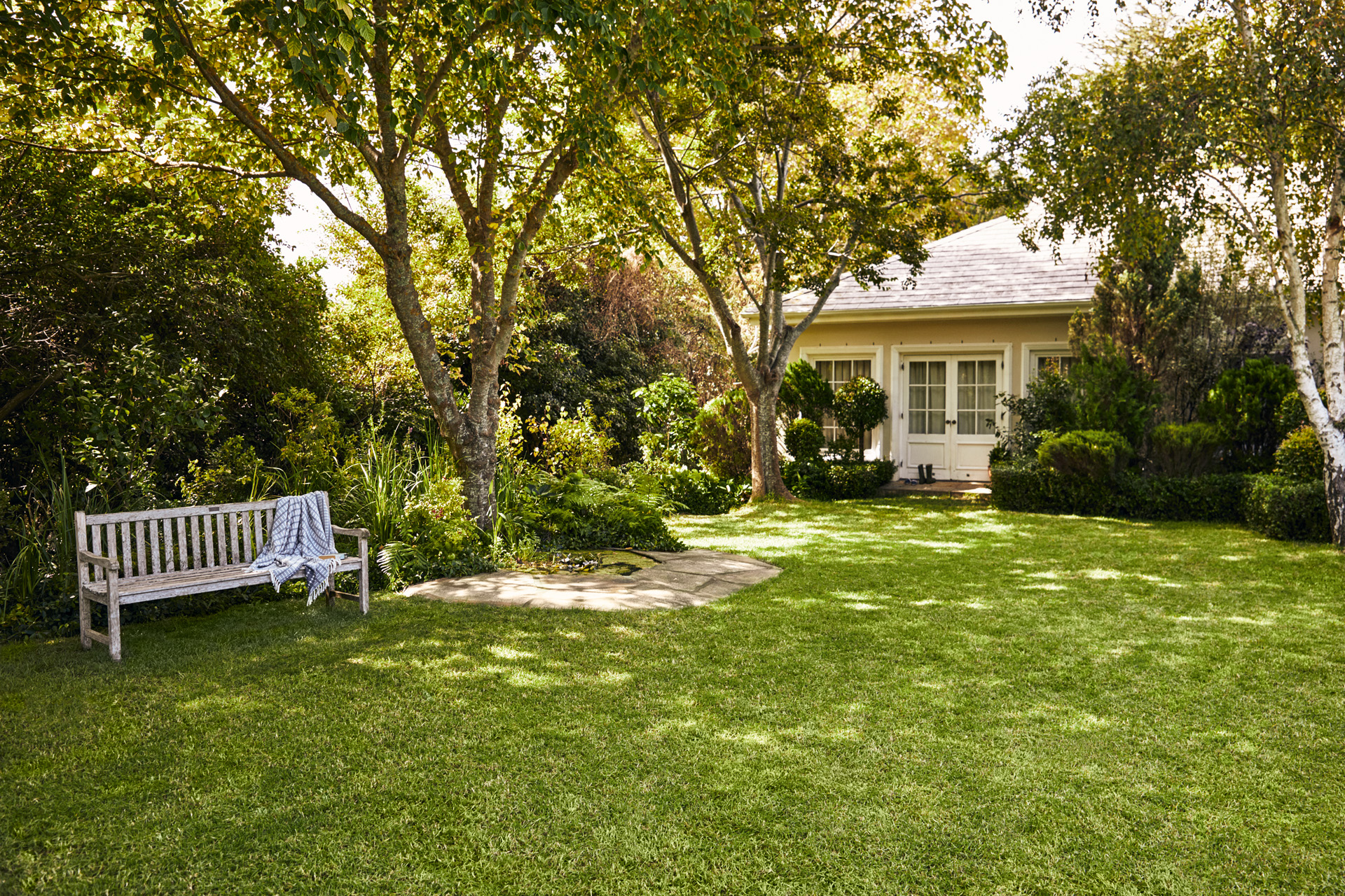Pequena casa com espaço verde; em primeiro plano, um banco de jardim sobre relvado verde