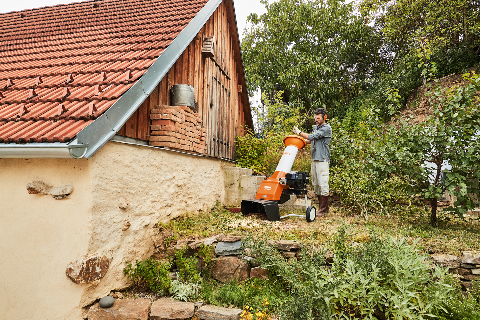 Um homem mostra como utilizar um biotriturador a gasolina STIHL GH 370 S num terreno, ao lado de uma casa