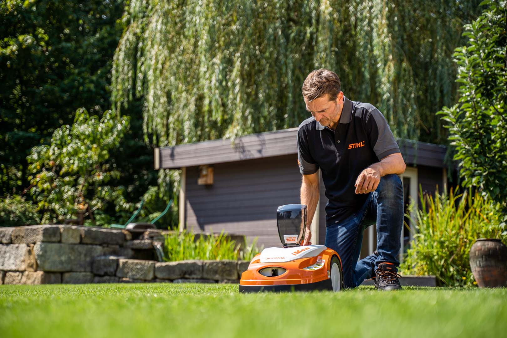 Um concessionário STIHL ajoelhado para ajustar as definições de um robot corta-relva STIHL iMOW® RMI 422 num jardim