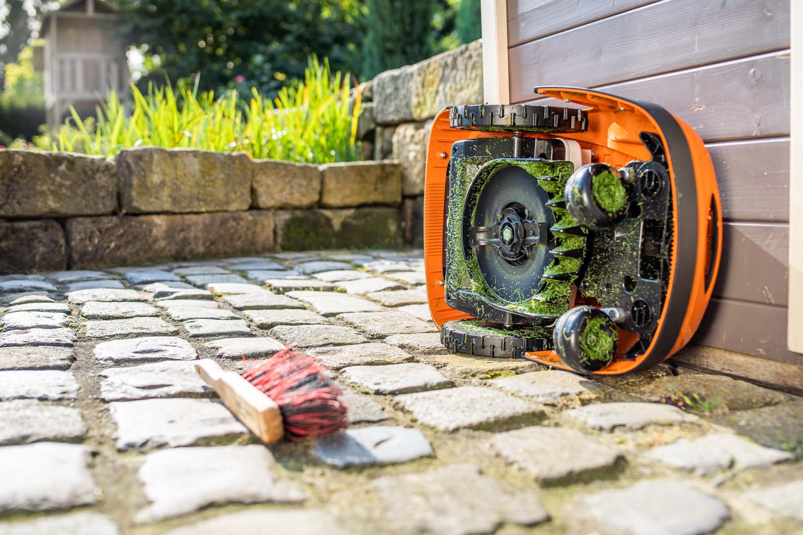 Preparação da limpeza do robot corta-relva STIHL iMOW®, deitado de lado, com uma escova no chão perto dele