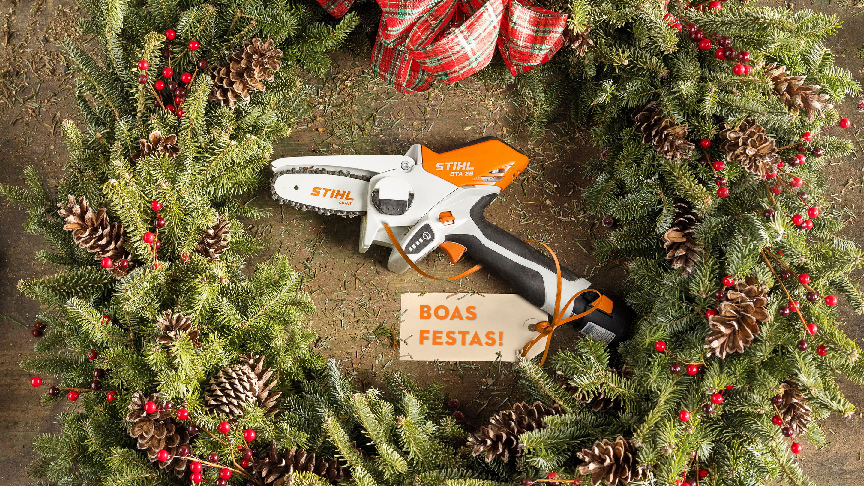 STIHL GTA 26 numa coroa de Advento, rodeada por ramos de pinheiro, pinhas e fita com cartão de Natal