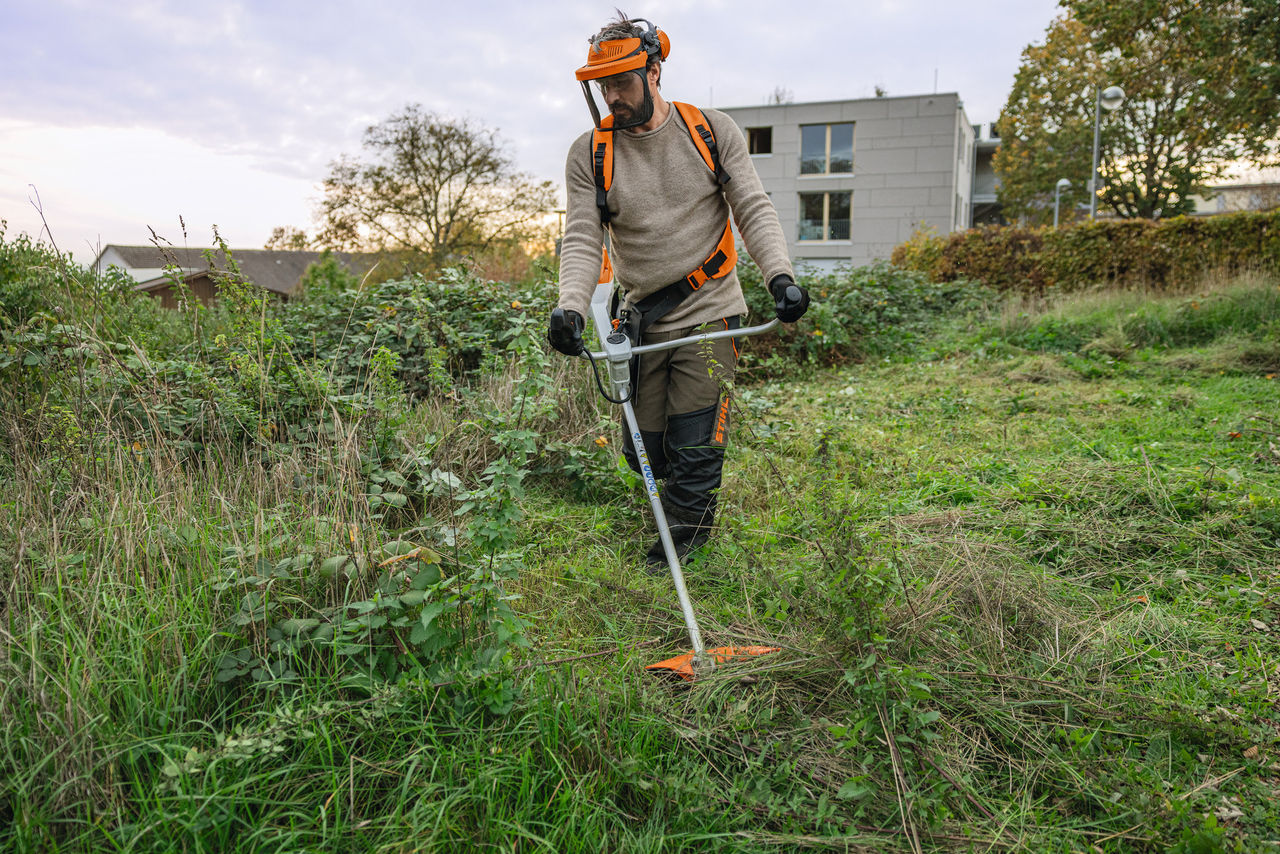 Um homem com equipamento de proteção STIHL a cortar a relva numa área verde selvagem com uma foice a motor a bateria STIHL FSA 200