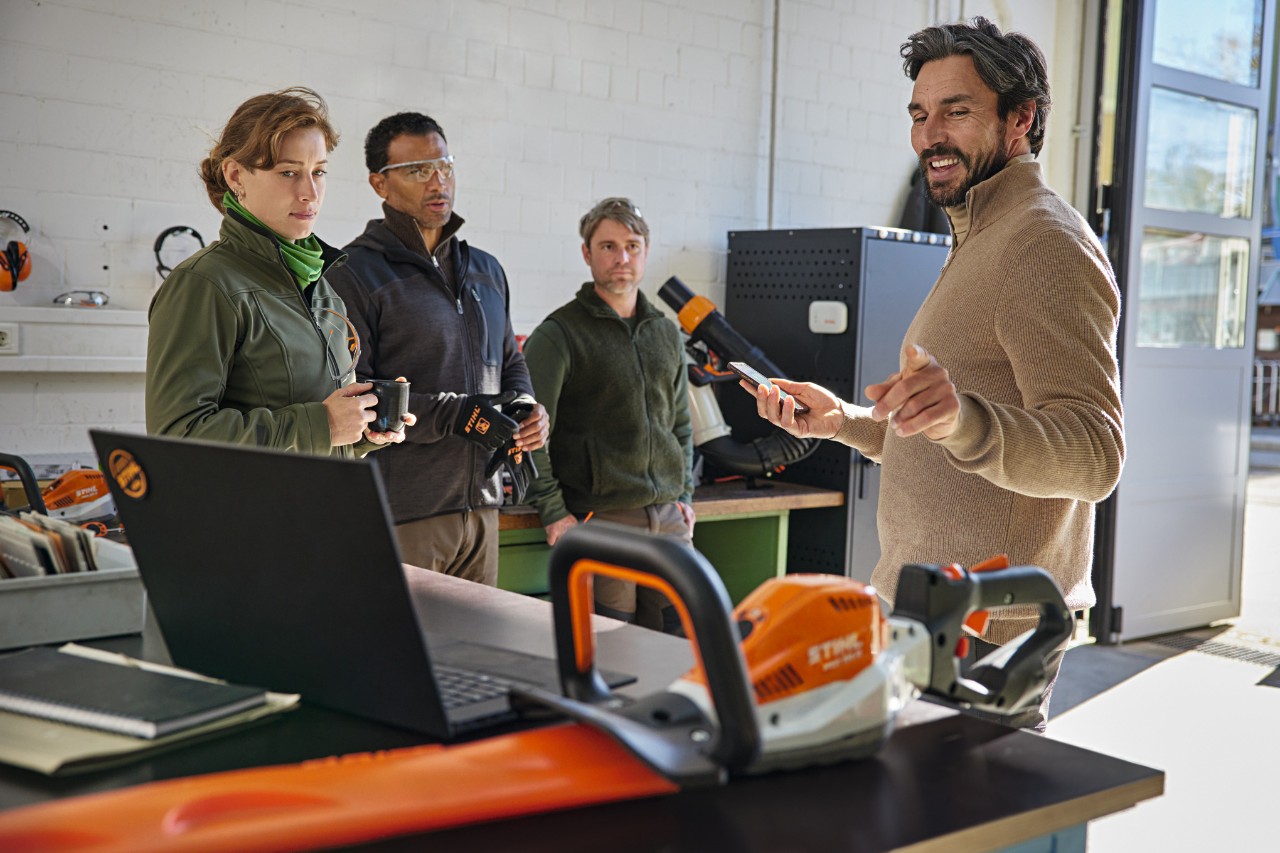 Uma equipa de paisagistas discute o seu trabalho num armazém com a ajuda da aplicação STIHL connected no seu smartphone