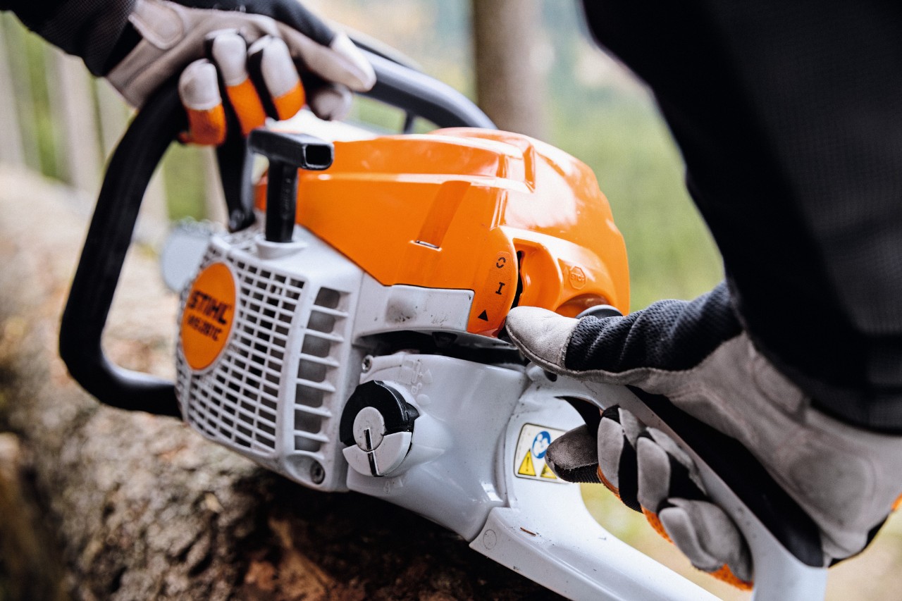 Grande plano de uma motosserra a gasolina STIHL MS 261 C-M a ser ligada por uma pessoa com luvas de proteção