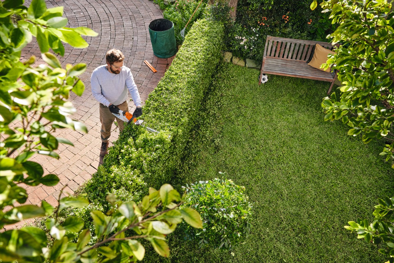 Um homem a cortar uma sebe no seu espaço verde com uma tesoura podadora de sebes STIHL HSA 40