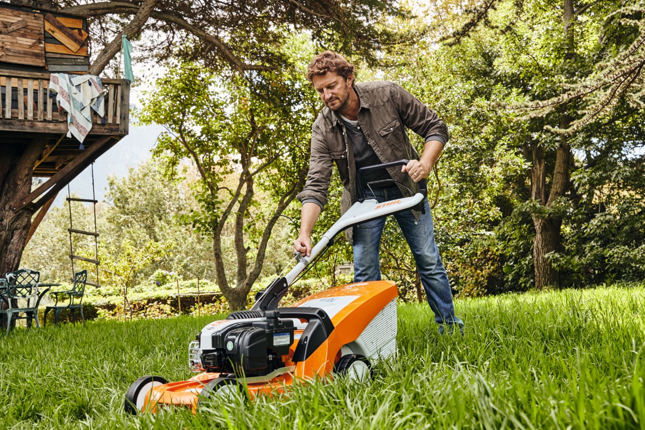 Um homem corta a relva num prado-jardim com um corta-relvas a gasolina STIHL RM 448 TC