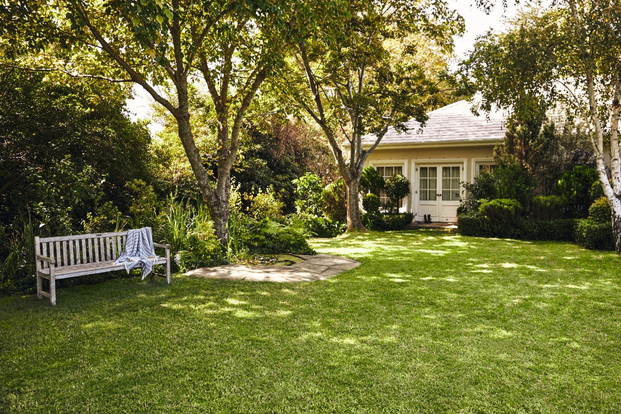 Pequena casa com espaço verde; em primeiro plano, um banco de jardim sobre relvado verde