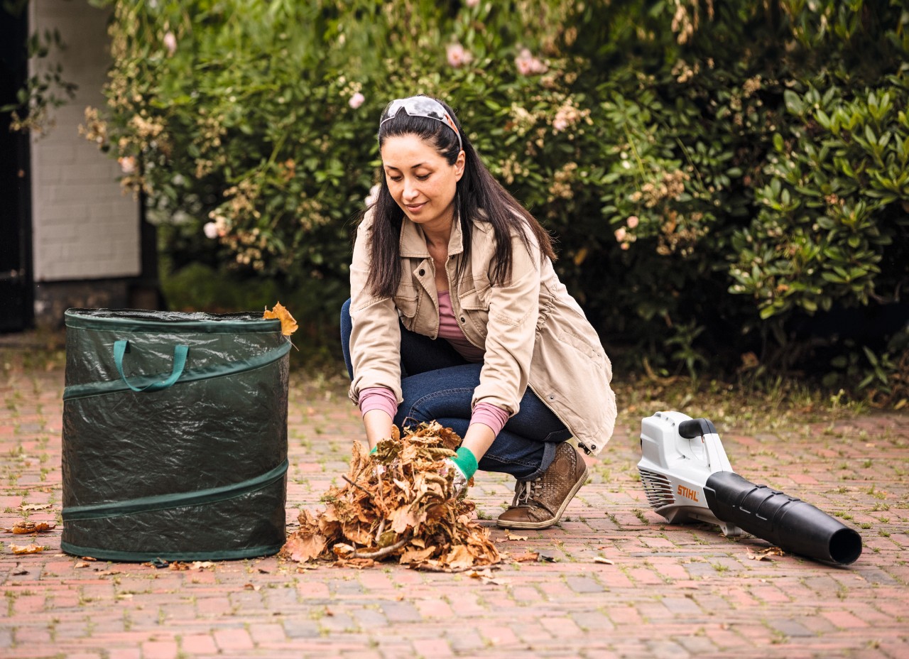 Mulher a eliminar folhas com a ajuda de um saco de folhas e de um soprador STIHL BGA 56